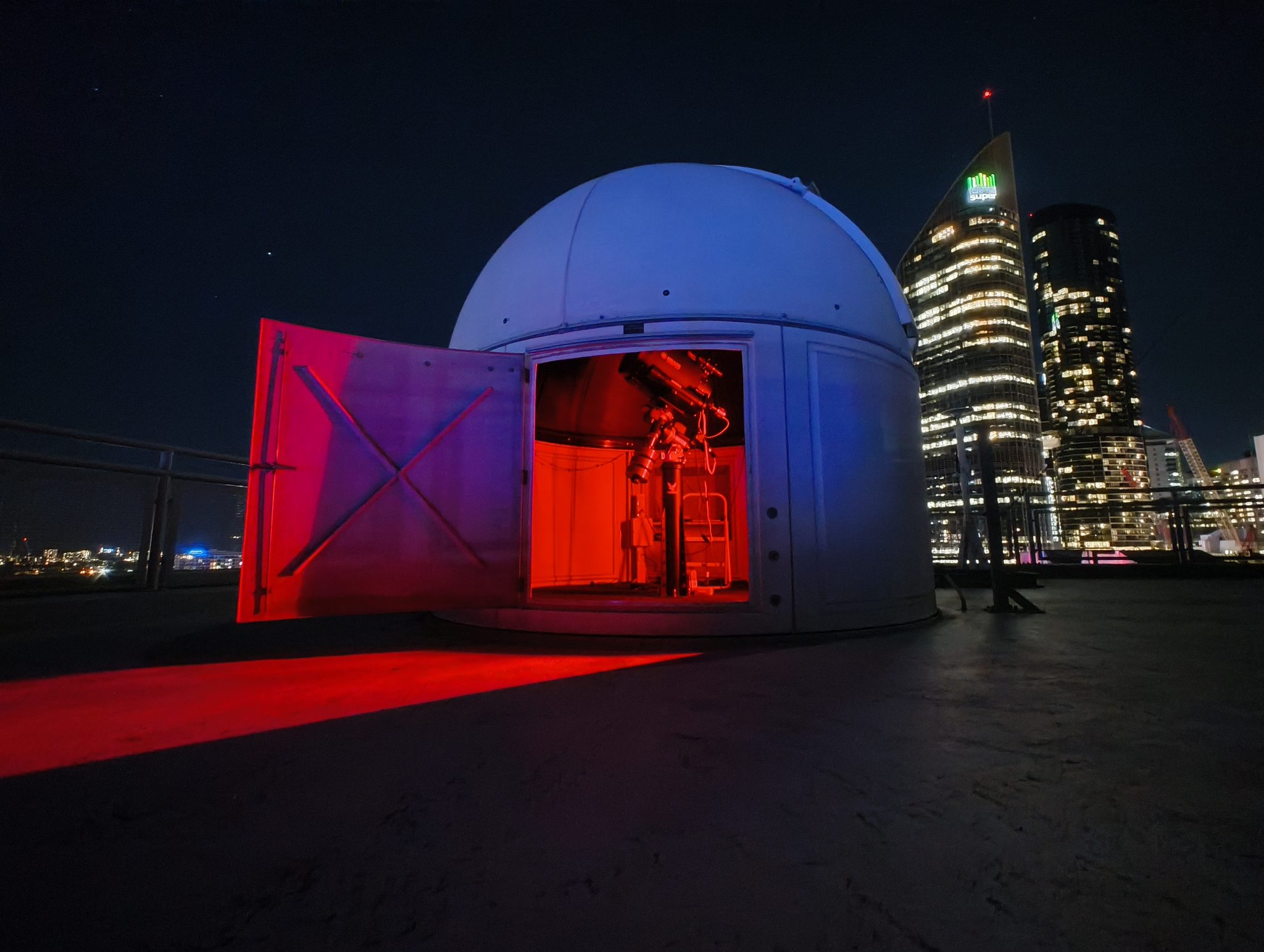 The QUT Astrophysics Observatory dome at Gardens Point, lit up at night with the Brisbane CBD skyline behind it